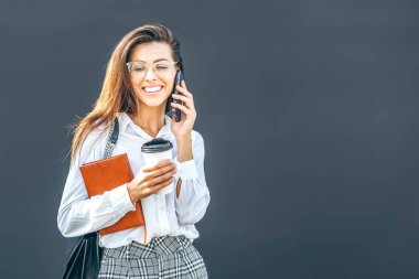 İş kadını cep telefonuyla yürüyor ve konuşuyor. Modern iş merkezinin yakınında. Not defteriyle.