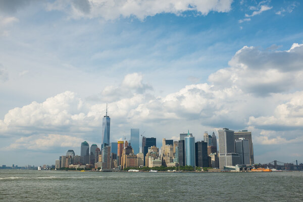 A view on the island of Manhattan, New York city, on a bright sunny day with some clouds. We can see the impressive building and skyscrapers.