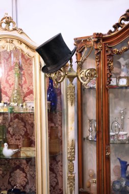 Antika mobilyaların arka planında şamdanda asılı duran klasik siyah erkek silindir şapkası.