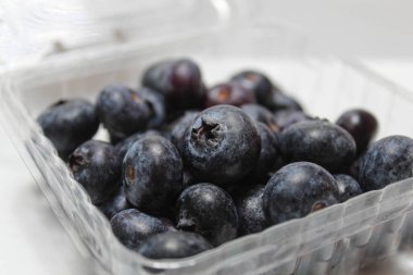 Şeffaf kutuda yaban mersini yığını, beyaz arka planda izole edilmiş.