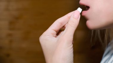 Kadın ağzının yanında bir hap tutuyor. Genç bayan ilaç alıyor. Kırpılmış