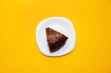 Tabakta çocuk oyuncağı, en iyi manzara. Süslü çikolatalı kek. Parlak sarı arka plan. Minimalizm