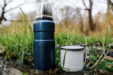 Akıntının yanında elektrikli süpürge ile kamp termosu. Yakın plan. Açık hava aktiviteleri, sıcak içecek, yürüyüş, seyahat.