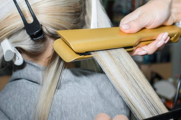 Keratin saçı profesyonel bir ütüyle düzeliyor. Kuaför kuaförlük yapıyor. Spa salonu konsepti, kuaförlük