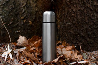 Ormanın dışında düşen meşe yapraklarının üzerinde duran vakumlu termos. Seyahat eden alüminyum matara. Seyahat, yürüyüş, macera, piknik kavramı.