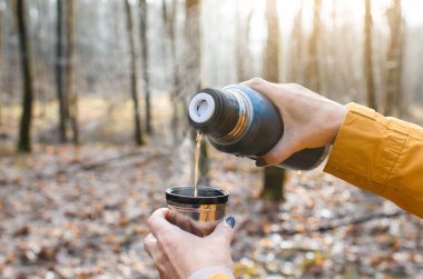 Yaşlı bir kadın termostan sıcak çay dolduruyor. Yaşlı bir kadının elinde, ormanda içkili bir kupa tutarken yakın plan..