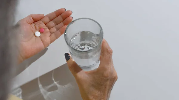 高齢女性は錠剤を飲む 水と薬のガラスを保持する女性の手のクローズアップ 白い背景コピースペース 治療の概念 病気の退職 — ストック写真