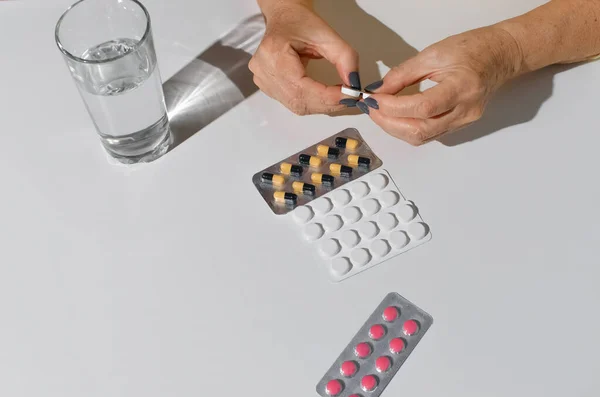 高齢女性の手の薬のパッケージを開く 白いテーブルの上の水の錠剤とガラス トップビュー — ストック写真
