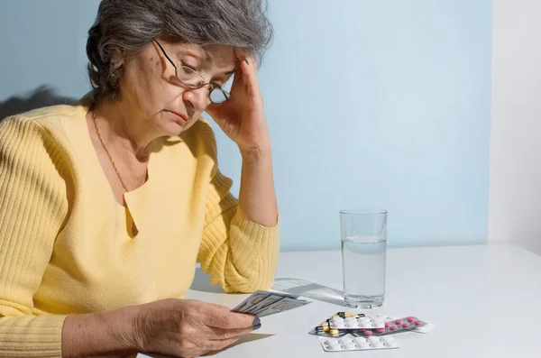 Elderly woman counting money for medical treatment. Pensioner sitting in the kitchen at the table with medicines. Concept of depression, price medicine, cost treatment.