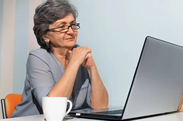 Laptopa bakan gülümseyen yaşlı kadın portresi. Seyahat, serbest çalışma, emeklilik kavramı.