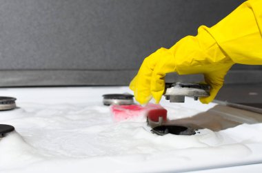 Kadın eldiveni, gaz sobasını kaldırıyor. Ev hanımı gaz sobasını sünger ve kimyasal köpükle temizliyor..