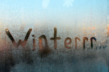 Winter frozen window. Creative spelling of the word Winter, means cold and freezing. Frosty pattern on glass, sunny morning. clipart