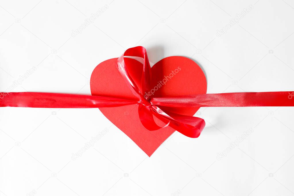 Red ribbon with a bow tied at the heart, flat lay. Concept heart as a gift.