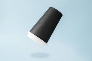 Tek kullanımlık kahve fincanı havada uçuşuyor. Açık mavi arkaplan. Metin için boş bardak yüzeyi