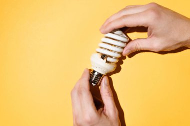 Yanmış bir ampulü tutan erkek eller. Sarı arkaplan, üst manzara. Elektrikçi kavramı