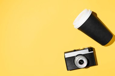 Klasik kamera ve tek kullanımlık kahve, düz konum. Sarı arkaplan, kopyalama alanı. Hippi Yürüyüş Kiti
