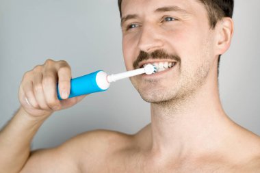 Modern elektrikli diş fırçasıyla gülümseyen bir adamın portresi. Diş fırçalayan adam, günlük hijyen prosedürü. Oral sağlık