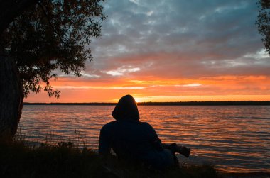Gün batımında göl kenarında dinlenen bir adam. Yalan söyleyen ve batan güneşe bakan kişinin silueti. Manzaranın keyfi ve tefekkürleri.