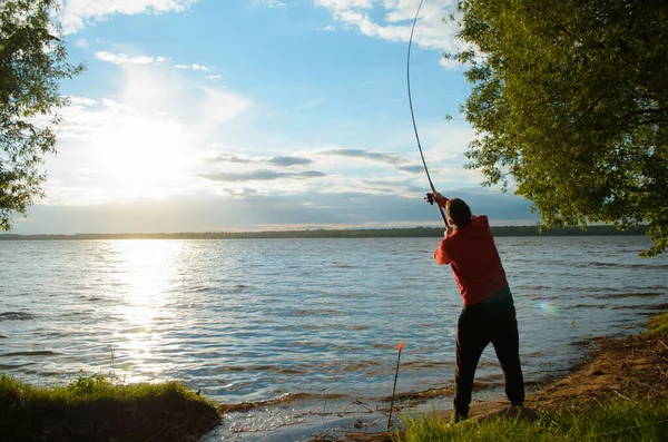湖の漁師 人は回転棒を投げ 後ろの眺め 日没時の釣り 木々の前に湖の海岸 — ストック写真