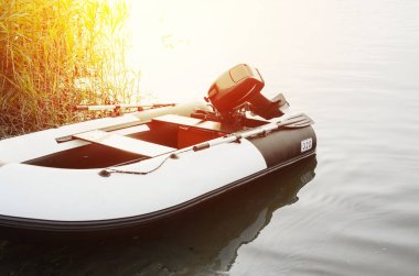 Güneşin doğuşunda ya da batışında, dışarıda, kıyıda şişme motorlu tekne. Sakin su, tekne motoruna özenli odaklanma. Balıkçılık konsepti, tekne gezileri