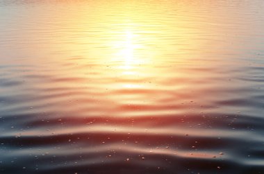 Gün batımında denize yakın çekim. Koyu mavi suyun sakin yüzeyi ve açık havada güneşten gelen sarı-kırmızı refleks. Arka plan manzara denizi, göl, köpüklü gölet. Doğal arkaplan kopyalama alanı, insan yok