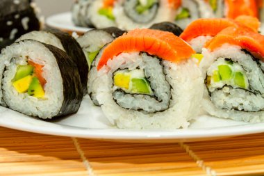 Lezzetli taze suşi, beyaz bir tabak ve siyah bir masa üzerinde. Japon mutfağı..