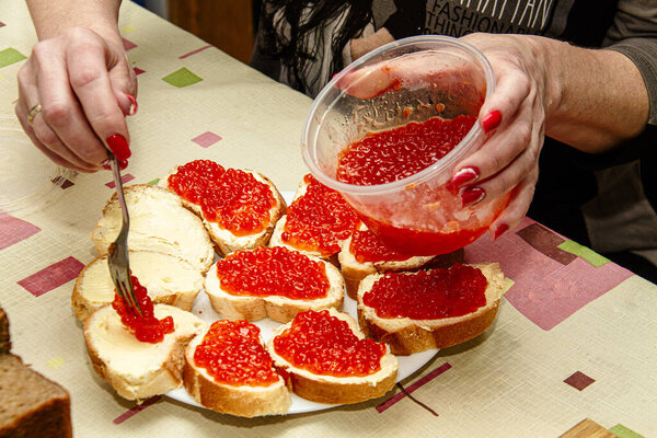 A woman spreads red caviar with a fork on a chopped baguette.