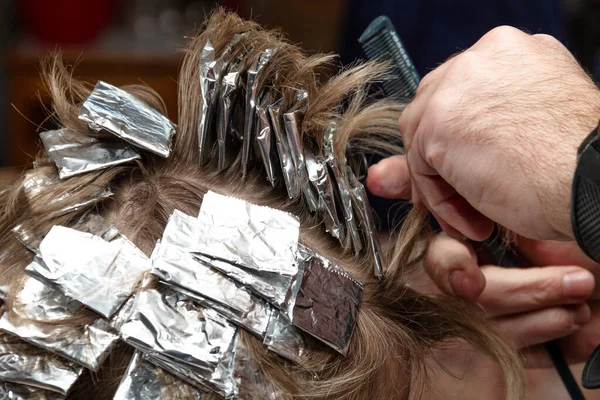Hairdresser makes hair coloring to a young woman. Close-up photo.