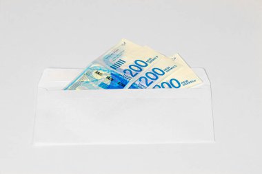 200 yeni İsrail şekelinin üç banknotu, arka planda hafif bir zarf ile bir posta zarfında..