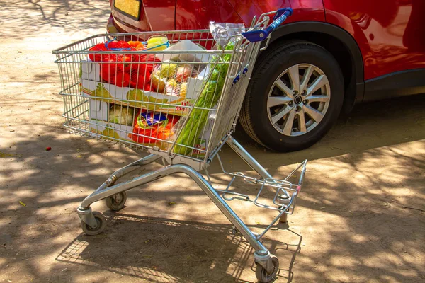 食料品でいっぱいのカートが車の隣の通りにあります — ストック写真