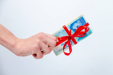 Bir adamın eli, açık arkaplanda kırmızı bir kurdeleyle bağlanmış 200 yeni İsrail şekeli banknotlardan oluşan bir tomar tutuyor.
