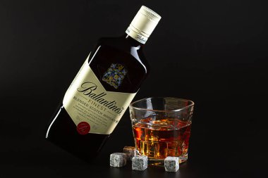 İsrail. Rishon LeZion. 08.14.2021. Bir şişe Ballantine viskisi, buzlu ve viski taşlı bir bardak viskinin üzerinde, siyah bir arka planda yatıyor..