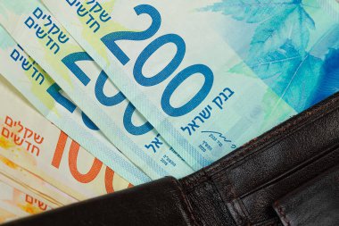 200 ve 100 İsrailli şekel banknotlar yakın plan deri bir cüzdandan sarkıyor.
