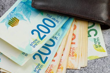 200 ve 100 İsrailli şekel banknotlar yakın plan deri bir cüzdandan sarkıyor.