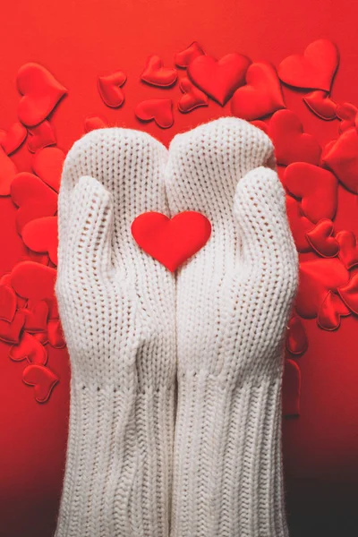 Hands in white knitted gloves hold red hearts on a colored background