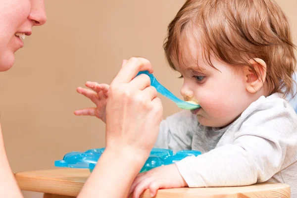 Moeder, baby voeden met een lepel aan de tafel. — Stockfoto