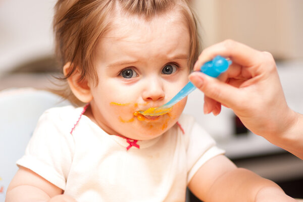 little girl feeding from a spoon on blue chair.