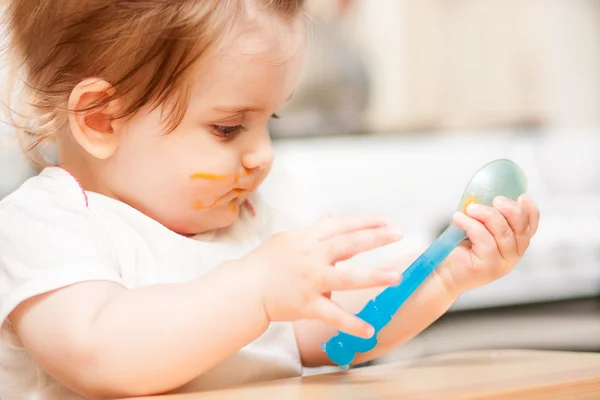 Little girl feeding from a spoon on blue chair. — Stock Photo, Image