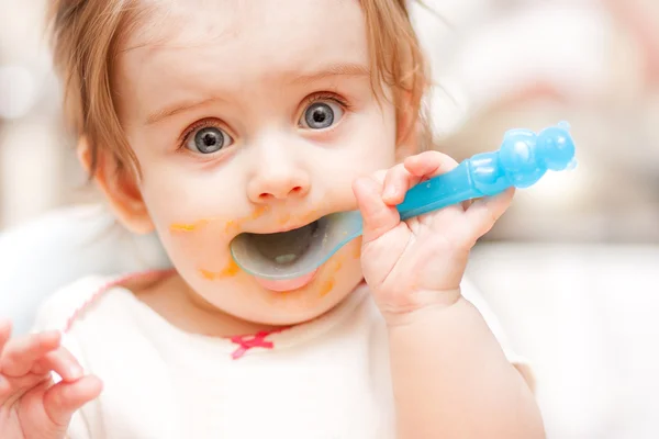 Little girl feeding from a spoon on blue chair. — Stock Photo, Image