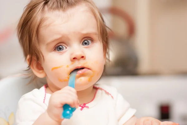 Little girl feeding from a spoon on blue chair. — Stock Photo, Image