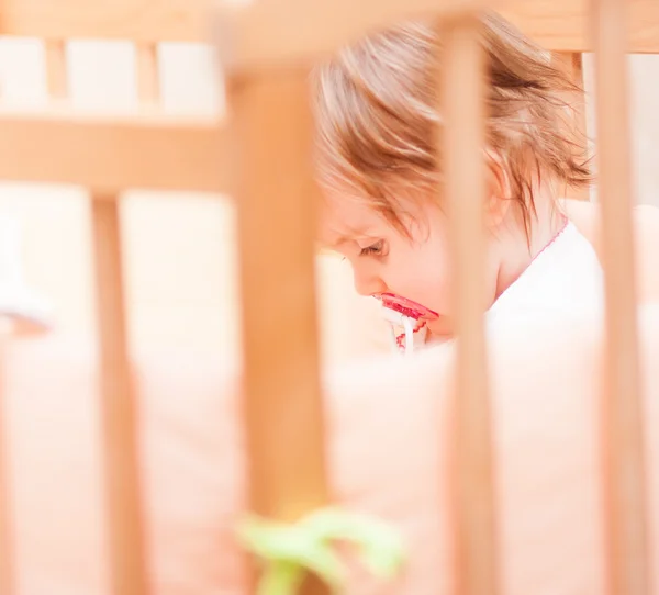 Little girl sitting in a crib with — Stock Photo, Image