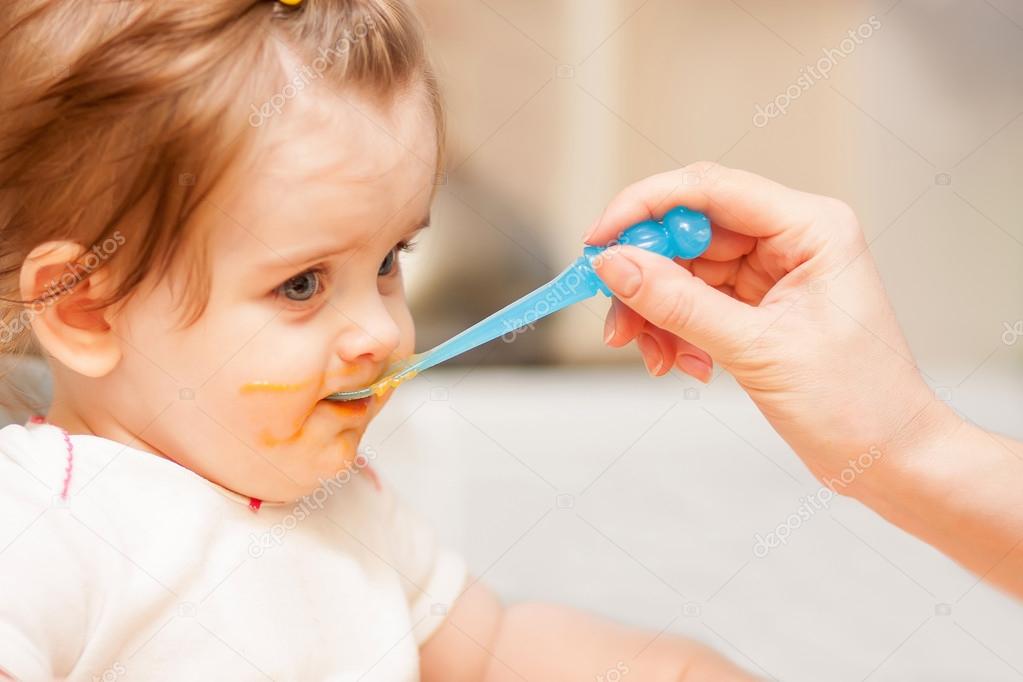 little girl feeding from a spoon on blue chair.