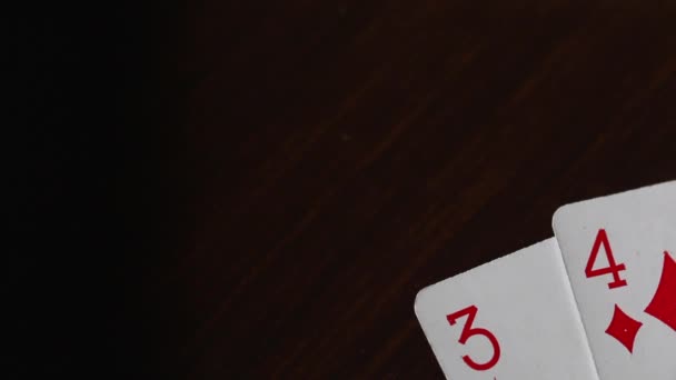 Würfel rollen auf der Oberfläche des Tisches. in der Ecke des Tisches befinden sich Spielkarten - drei- und vierfach rote Farbe. Würfel weiß mit schwarzen Punkten. Videoaufnahme aus nächster Nähe auf einem Canon 70d — Stockvideo