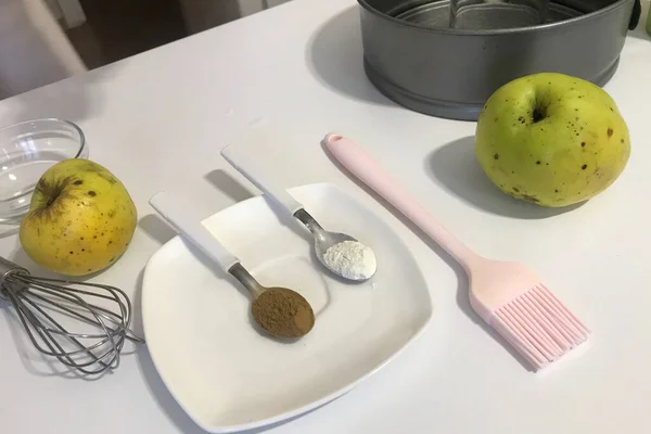 Cinnamon and baking powder in teaspoons. On the table are ingredients and tools for making charlotte. Autumn pie with apples.