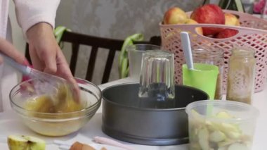 Bir kadın çırpıcı ile Charlotte hamur karıştırıyor. Yakınlarda elmalı turta yapmak için aletler ve malzemeler var..