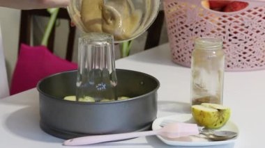 Bir kadın hamuru Charlotte 'un pişirme kabına döküyor. Elma dilimlerinin üstünde. Yakın plan..