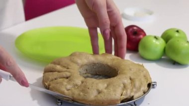 Kadın pişmiş Charlotte 'u biçimden ayırıyor. Yakınlarda birkaç elma var..