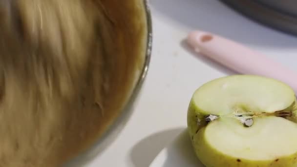 Une femme mélange la pâte à charlotte avec un fouet. La moitié d'une pomme se trouve à proximité. Gros plan. — Video