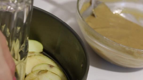Жінка кладе шматочки яблука в блюдо для випічки Шарлотти. Поруч з ним знаходиться тісто з яблучним пирогом. Крупним планом . — стокове відео