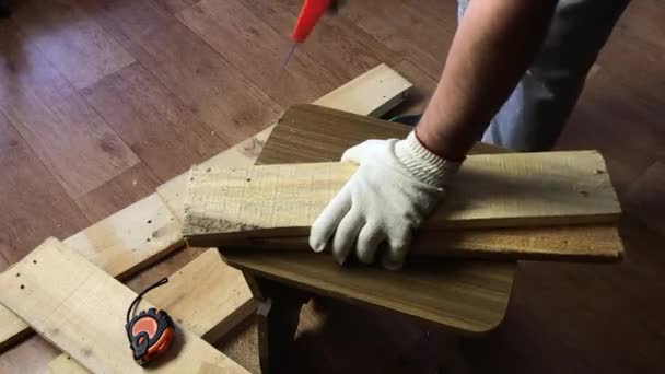 Een man zaagt planken met een ijzerzaag en vouwt ze samen. Maakt een opbergdoos voor het oogsten van groenten. Groenten oogsten tijdens de epidemie in een stadsappartement. — Stockvideo